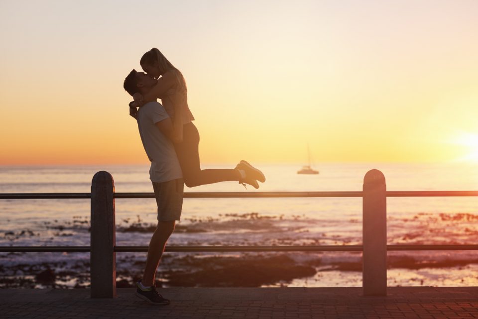 Young woman jumps into boyfriend's arms and gives him a kiss at sunset