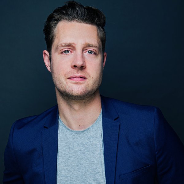 A headshot of Max Dickins wearing a blue suit